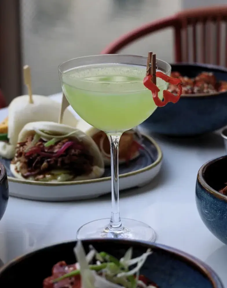 A green summer cocktail garnished with red chilli at Amazing Grace Canary Wharf, served alongside Pan-Asian sharing plates including bao buns on the outdoor terrace