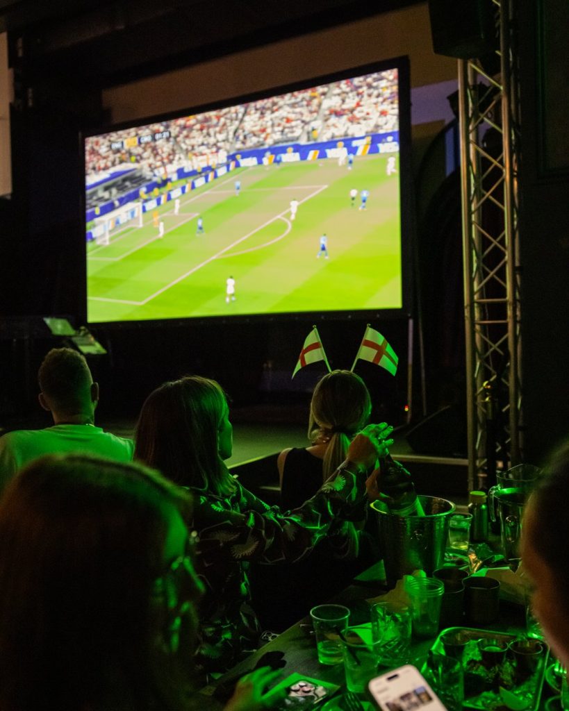 England fans with St George's Cross flag headbands watching World Cup on big screen at Amazing Grace Canary Wharf